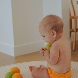 A baby sitting on a Rug with Retro Wave By Ina - Lumi Brief Swim Nappy - Dandelion.